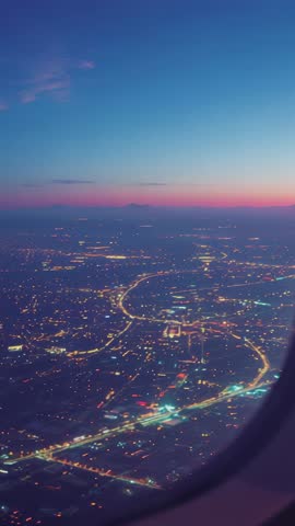 Vertical Aerial Descent Showing City Lights and Highways Through Airplane Window at Dusk