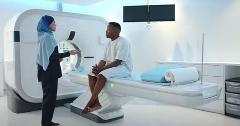 Female radiology technologist in hijab consulting african american patient on mri table