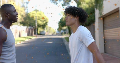 Young Men Confronting Each Other on Suburban Street with Suspended Orange Light Particles