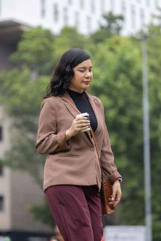 Urban professional walking with coffee holding crossbody bag wearing blazer and officewear