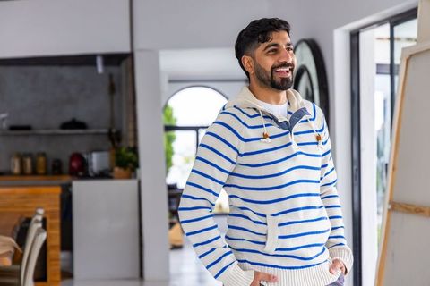 Smiling man wearing striped sweater standing in sunlit modern kitchen with blank canvas