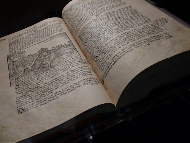 Old book opened to show its pages with illustrations and text under low light. Useful for themes of history, vintage books, antique literature, archaeological studies, and medieval manuscripts.