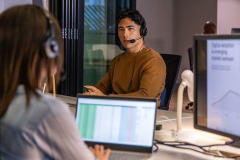 Customer support team collaborating in open-plan office with asian agent on headset