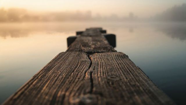 Weathered wood pier leading into misty lake dawn with warm golden sun reflections