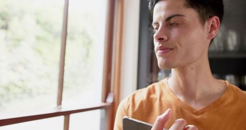 Young Biracial Man Contemplating Using Tablet by Bright Window