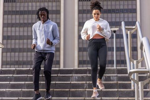 Urban fitness duo running down concrete steps wearing leggings and hoodies, city workout