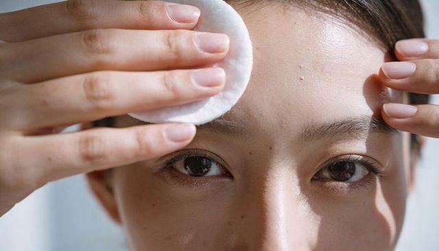 Asian woman cleansing forehead with cotton pad closeup, skincare routine and beauty care