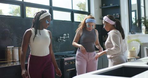 Diverse friends wearing under-eye patches and headbands while chatting in modern kitchen