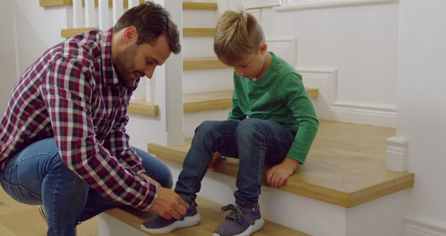 Happy caucasian father with son tying his shoes on stairs at home. Domestic life, family and lifestyle, unaltered.