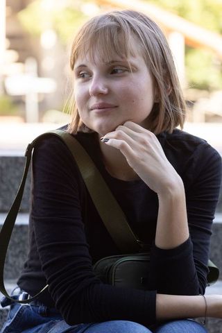 Young woman sitting on stone steps wearing black top and denim holding olive-green crossbody bag