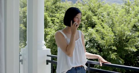 Asian Woman Talking on Smartphone on Sunny Balcony