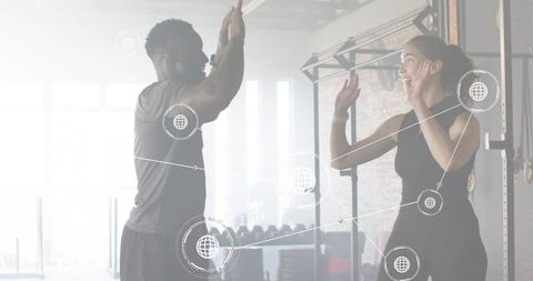 Trainer high-fiving client in bright gym with virtual network overlay and free weights