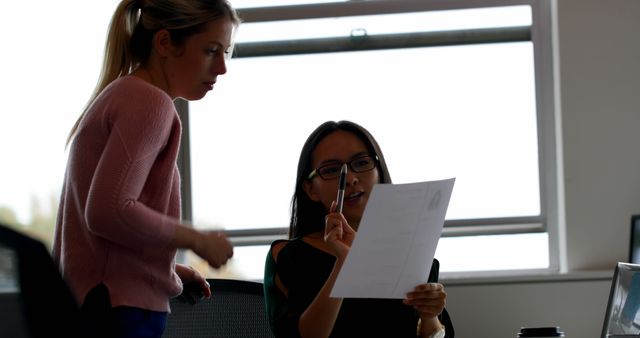 Female colleagues working together in modern office, reviewing document, discussing project details. Ideal for business-related content, teamwork depictions, collaborative work environments, corporate presentations, or career-focused materials.