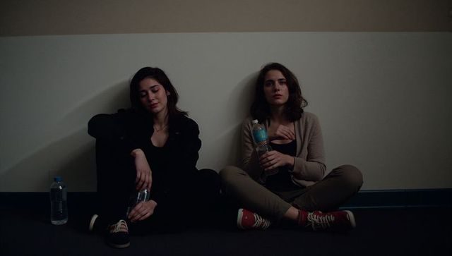 Two young women sitting against wall holding water bottles late-night quiet moment