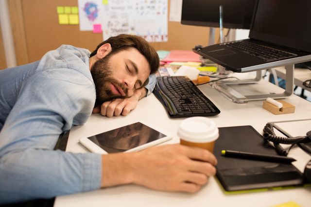 High angle view of tired businessman napping on desk in creative office