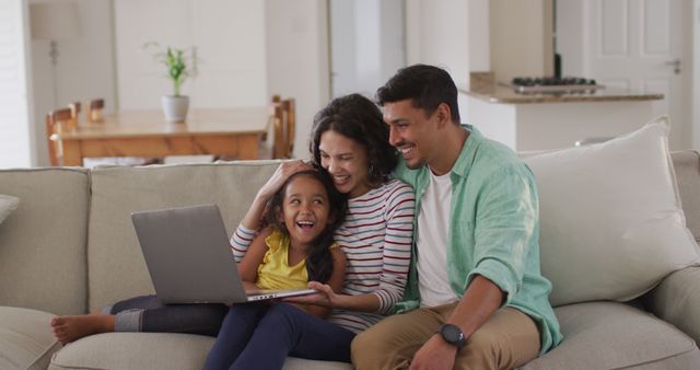 This image shows a happy family with parents and a child sitting on a sofa in a living room, using a laptop. The casual and comfortable atmosphere suggests a relaxed family bonding moment. Ideal for marketing campaigns related to family values, home life, technology, and internet services. Can be used in blogs, advertisements, and social media to depict family lifestyles and home activities.