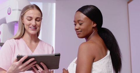 Nurse explaining mammogram procedure to patient using tablet in clinic exam room