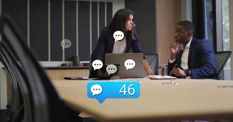 Leaning executives discussing laptop with message notifications showing 46 in boardroom