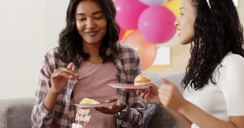 Two Women Enjoying Cake at a Birthday Celebration with Balloons