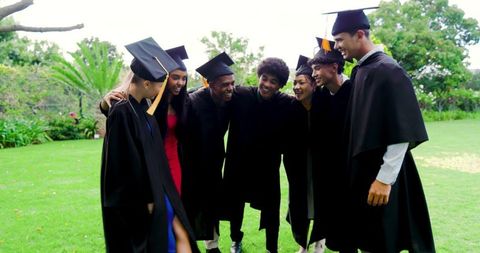 Diverse Graduates Celebrating on Campus Lawn Smiling in Caps Gowns and Colorful Dresses