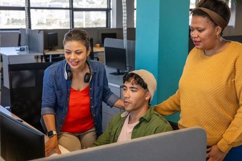 Diverse team collaborating at shared workstation with monitors and headphones in modern office