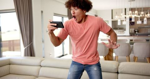 Surprised man holding smartphone reacting to news at home