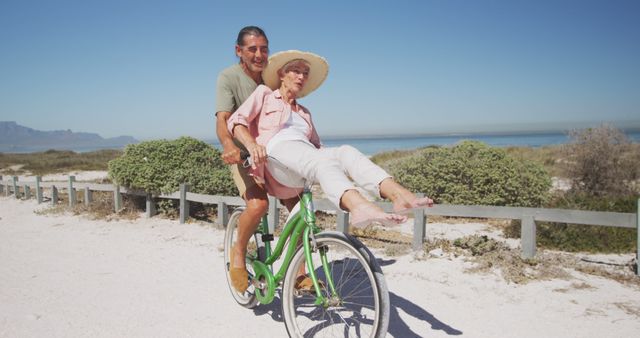 Elderly man and woman having fun on green bike at sandy beach, woman's feet joyfully raised in air. Ideal for retirement lifestyle promotions, senior health club advertisements, and outdoor activity ideas for older adults. Captures essence of fun and adventure in later years.