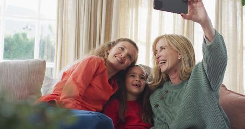 Smiling grandmother taking selfie with daughter and granddaughter on cozy sofa