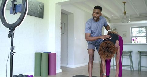 African american trainer guiding female client through forward bend during home workout