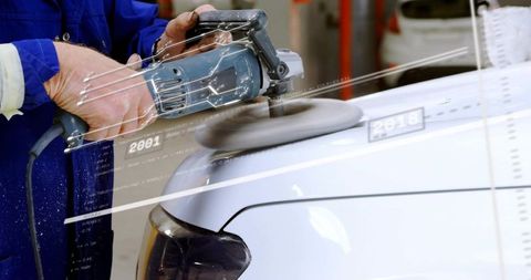 Close-up mechanic polishing white car hood with orbital polisher in busy auto workshop