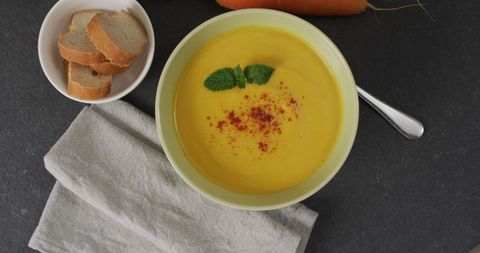 Bowl of creamy carrot soup with bread and fresh vegetables