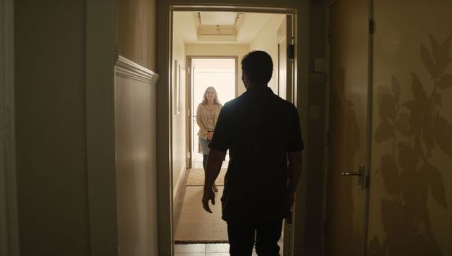 Man walking toward woman smiling at open front door in sunlit narrow hallway