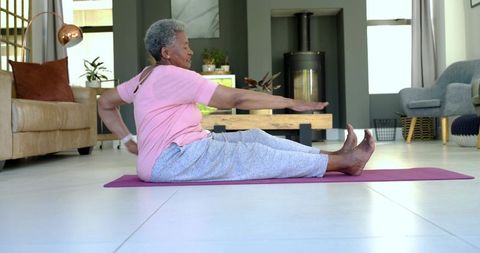 Senior woman stretching on yoga mat in bright living room with smartwatch and serene decor