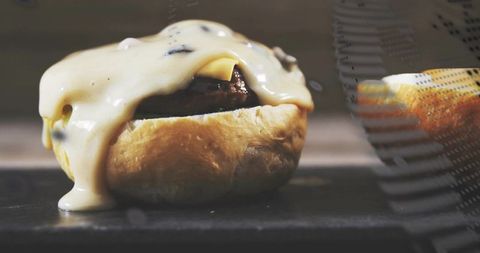 Melting cheese dripping over juicy beef slider on hot griddle closeup