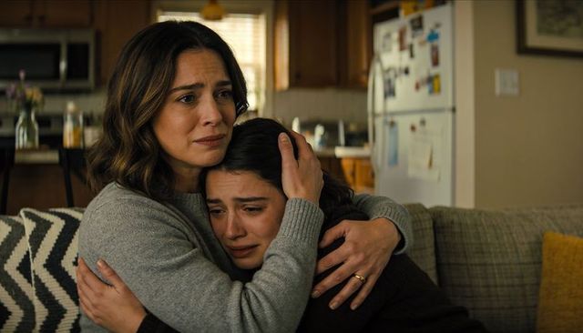 Mother comforting crying teenage daughter on couch in cozy open-plan kitchen interior