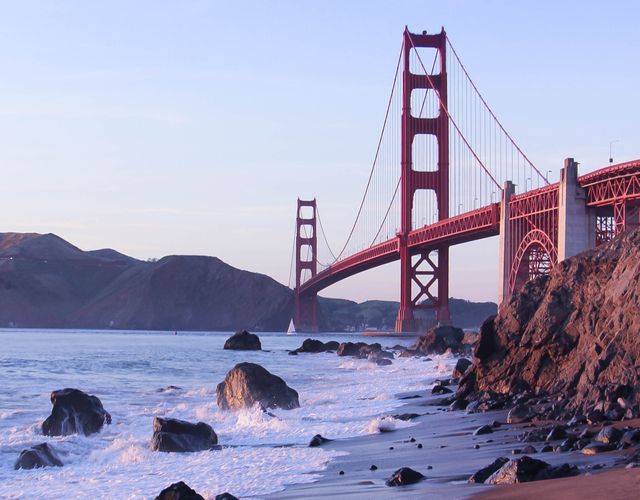 This stunning view of the Golden Gate Bridge during sunset captures the iconic structure with waves crashing on a rocky beach. Perfect for travel guides, tourism advertisements, and architectural showcases. This image emphasizes the majestic beauty of San Francisco's most famous landmark, highlighting its global appeal to visitors.