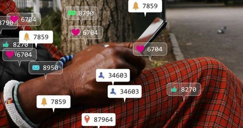 Man scrolling smartphone with social notifications near tree wearing red plaid and beaded bracelets