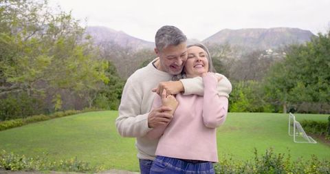 Mature Couple Hugging in Garden Wearing Sweaters with Scenic Mountain View
