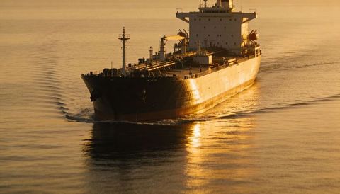 Gliding crude oil tanker at golden hour reflecting warm amber light across ocean surface