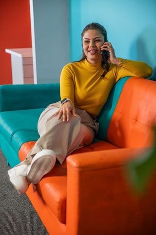 Young professional relaxing on colorful office couch talking on phone with smartwatch