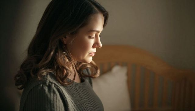 Young woman sitting on bed gazing downward in warm soft light, intimate bedroom portrait