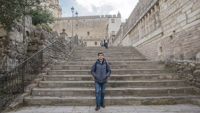 Young man standing at foot of historic stone staircase in medieval european plaza