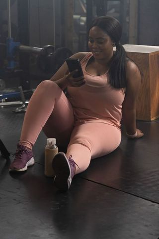 African american woman resting after workout wearing pink activewear using smartphone