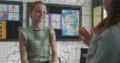 Girl learning with tutor, equations and graphs on clear glass board, classroom tutoring scene