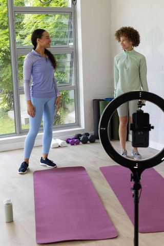 African american women filming home workout session on yoga mats with ring light