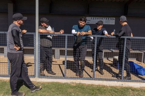 Baseball teammates chatting and leaning on dugout fence during sunny amateur practice