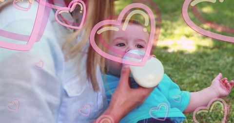 Mother feeding baby boy outdoors with heart overlays expressing love