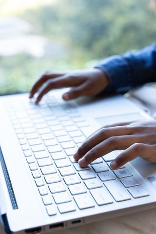 African american hands typing on white laptop keyboard with denim sleeves by window