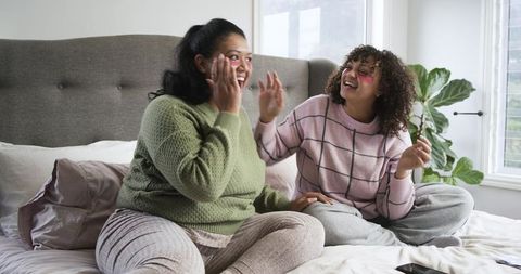 Mother and daughter enjoying cozy skincare moment on bed with playful pink under-eye masks