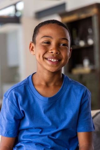 Smiling school-age boy wearing blue t-shirt sitting on couch in cozy living room portrait